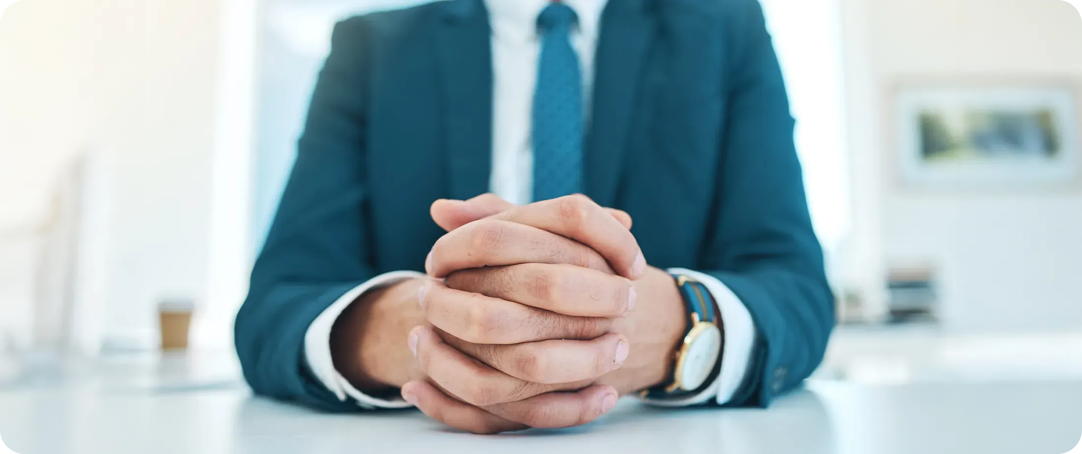 A lawyer in a dark blue suit sits at a white desk with hands clasped, conveying composed professional judgment