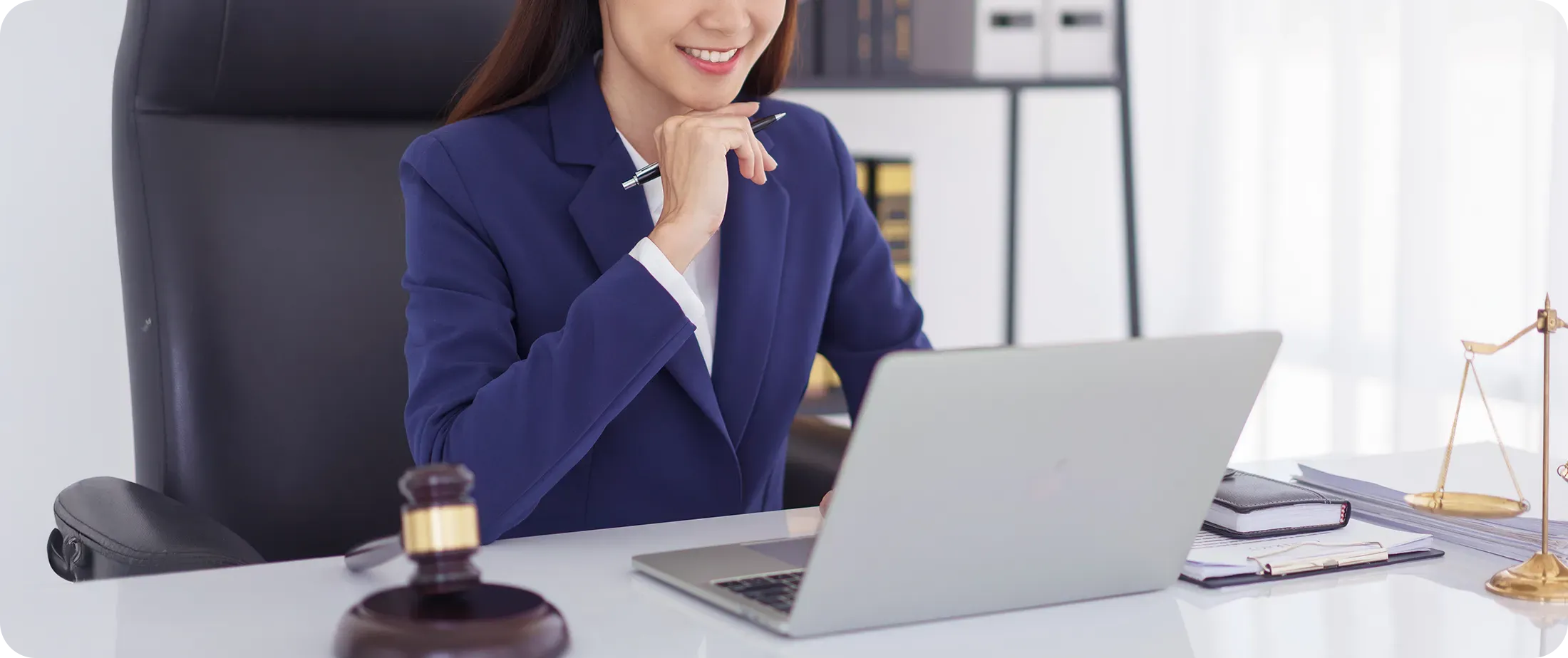 Legal professional reviewing media coverage on laptop, with gavel and scales of justice on desk
